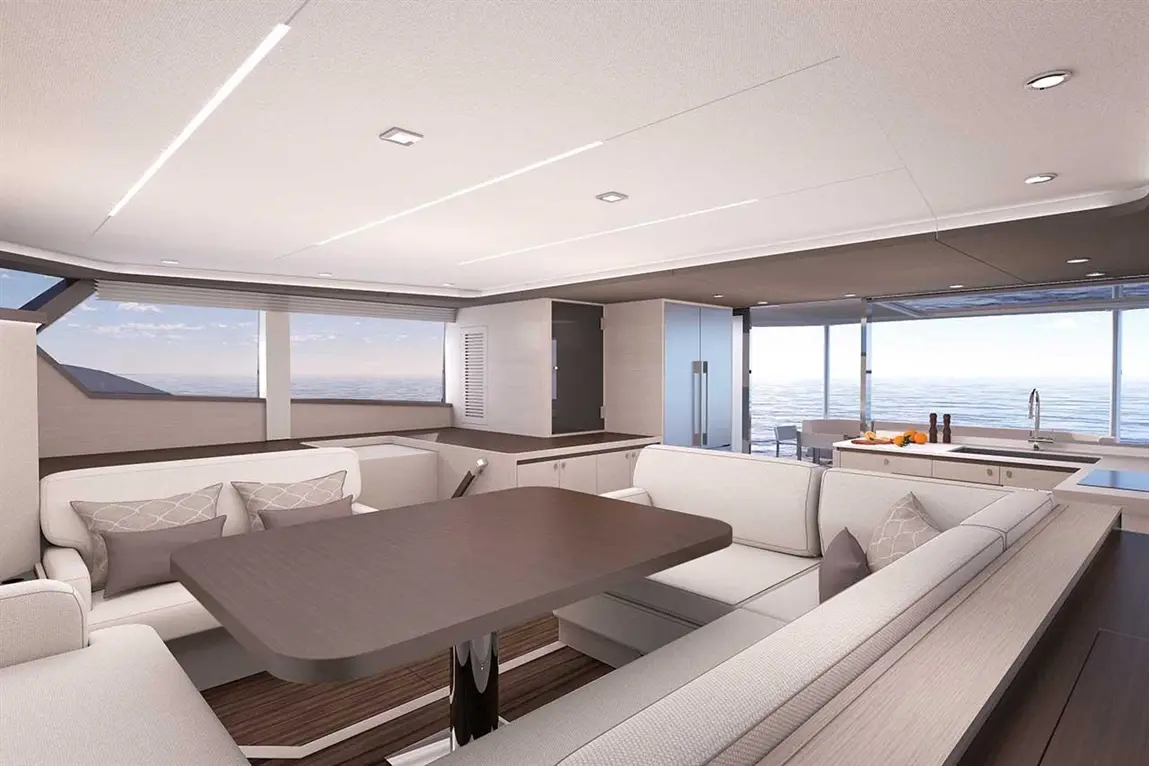 Modern yacht interior with a dining area, plush seating, and a kitchen, featuring panoramic ocean views through large windows.